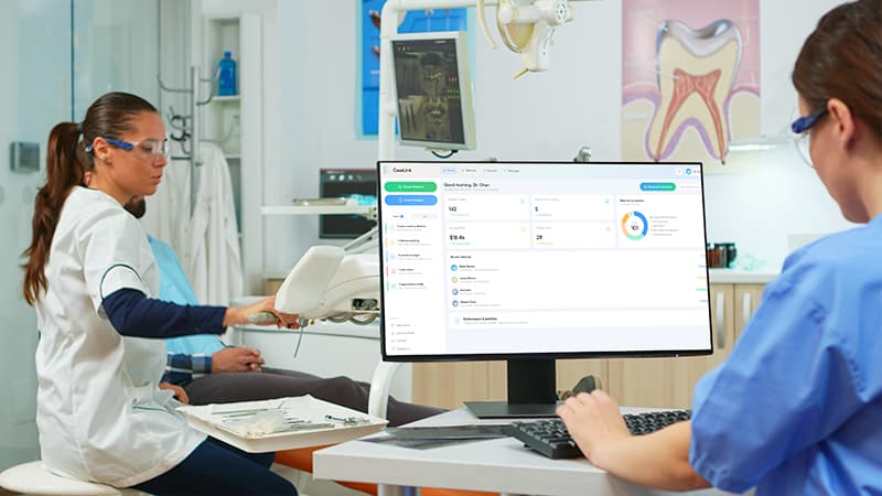 A dentist and patient view a screen together at the chair, reviewing care information.